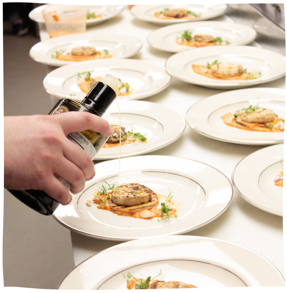 a row of plates in kitchen prep getting the finishing touch before being served